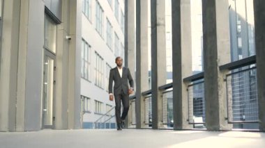 Kendine güvenen Afrikalı Amerikalı iş adamı modern şehirde yürüyor. Resmi giyinmiş profesyonel bir erkek ofis binaları dışında hareket ediyor. Kentsel çevre, kararlılık ve başarı