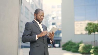Kendine güvenen Afrikalı Amerikalı işadamı, şehir sokak ortamında tablet kullanıyor, cihazla etkileşime giriyor, işine odaklanıyor. İş adamı erkek profesyonel teknolojisi ofis yakınlarındaki açık havada kullanılıyor.