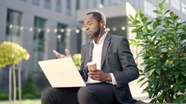 Takım elbiseli Afro-Amerikan bir adam bilgisayar kullanarak dışarıyı arıyor. İş adamı kahve fincanı tutuyor ve şehir merkezindeki toplantı sırasında kulaklık takıyor.