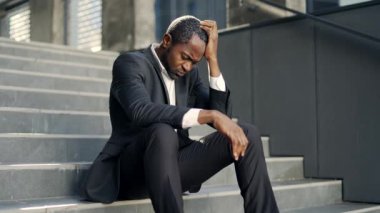 Afrikalı Amerikalı işadamı basamaklarda oturmuş hayal kırıklığı içinde başını tutuyor. Takım elbiseli iş adamı stres, endişe ya da başarısızlık yaşıyor. Şehir profesyoneli dışarıda duygularla boğuşuyor.