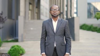 Kendine güvenen Afro-Amerikan resmi takım elbiseli adam şehir ofis ortamında karşıdan karşıya geçiyor. Başarının ve liderliğin resmedildiği profesyonel bir portre. İş adamı dışarıdaki kameraya bakıyor.