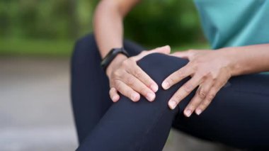 Afro-Amerikan sporcu kadın şehir parkında diz kaslarına masaj yapıyor. Siyahi kadın travma yarasından muzdarip. Fitness dişisinin burkulması şiddetli ağrı germe kuvveti. Bacağa kramp girdi. Baldır sporu.