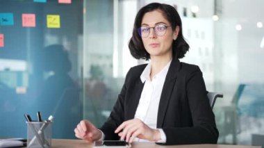 Webcam görüntüsü. Modern ofisteki kendine güvenen iş kadını çevrimiçi konferansı dizüstü bilgisayarla dinliyor. Bir kadın işçi masaya oturur ve kameraya bakarken sanal toplantı veya eğitim oturumuna katılır.