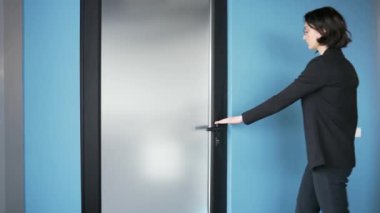 Siyah takım elbiseli kadın bir ofis çalışanı cam kapıyı açıyor. Ofise giren profesyonel bir kadın. Modern kurumsal ortamda tasvir edilen kişi giriş yapıyor. Yeni fırsatlara giriş kavramı