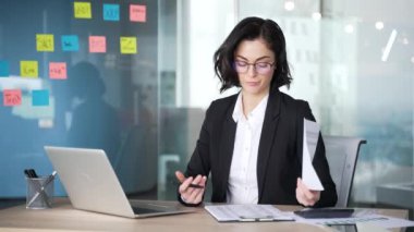 Modern ofiste mali belgeleri inceleyen bir iş kadını. Mali sonuçlardan kafası karışmış gibi görünüyor. Masada dizüstü bilgisayarla çalışan gözlüklü ve takım elbiseli bir profesyonel. İş stresi