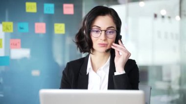 Sanal toplantı yaparken kulaklık takan kendinden emin kadın müşteri hizmetleri temsilcisi. Modern iş ofisindeki dizüstü bilgisayarla internetten iletişim kuran profesyonel bir kadın. Kapat. 