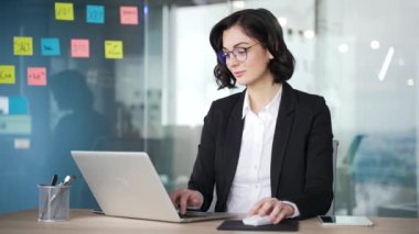 İş yerinde dizüstü bilgisayarla oturan, gözlüklü, kendine güvenen iş kadını. Profesyonel kadın işçi toplantı ya da proje planlamaya hazır. Kameraya bakan başarılı menajerin vesikalığı