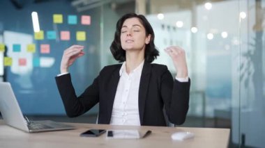 İş kadını stres atmak için çalışma masasında farkındalık meditasyonu yapıyor. Siyah takım elbiseli sakin kadın ofis çalışanı gözlerini kapatıyor ve kurumsal çevrede nefes almaya odaklanıyor.