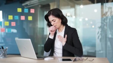 İş saatlerinde öksürük ve soğuk yüzünden acı çeken kadın ofis çalışanı. İş yerindeki masasında sandık başında oturan profesyonel giysili kadın solunum hastalığından rahatsız olduğunu gösteriyor.