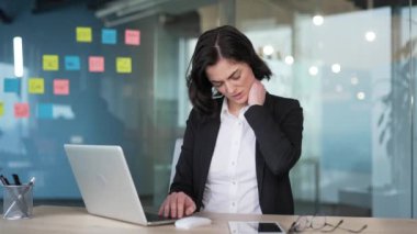 Modern ofiste dizüstü bilgisayar kullanırken boynu ağrıyan iş kadını kıyafeti. Mesleki çalışmayla ilgili stres ve rahatsızlık, ofis çalışanlarının karşılaştığı sağlık sorunlarını vurguluyor