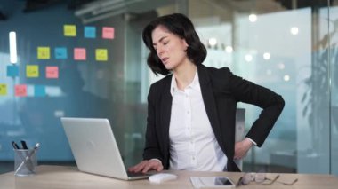 Masasında sırt ağrısı çeken, rahatsız edici bir ifadeyle oturan bir kadın. Dişinin iş stresi ya da duruşuyla ilgili sorunları var. Profesyonel bir insan iş yerinde acı ve rahatsızlıktan muzdariptir.