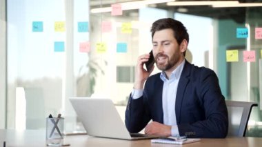 Kendine güveni tam bir işadamı, modern ofisteki iş yerinde akıllı telefondan konuşuyor. Resmi takım elbiseli bir işçi bir müşteriyle telefon görüşmesi yapıyor ya da iş ortağıyla sohbet ediyor.