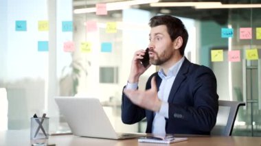Takım elbiseli kızgın işadamı iş yerindeki iş yerinde telefonda konuşurken tartışıyor. Heyecanlı yönetici, çözülmesi gereken sorunlar hakkında astlarıyla duygusal olarak konuşuyor.
