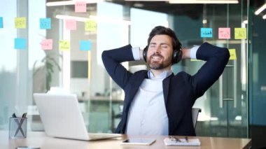 Ofis koltuğunda oturup kulaklıkla müzik dinleyen bir iş adamı. Neşeli erkek gözlerini kapar ve zevk alır. İş molalarında rahatlama ve sükunet stres atma ve keyif alma kavramı