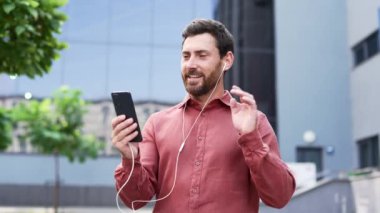 Sakallı adam ofis dışında görüntülü konuşma yapmaktan hoşlanıyor. Kendine güveni tam bir işadamı konuşurken gülümser, şehir merkezinde akıllı telefon tutar. Profesyonel çalışan telefonla iletişim kuruyor. Çevrim içi sohbet