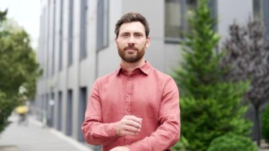 Ofis binasının dışında kolları bağlı duran kendine güvenen sakallı iş adamının portresi. Gülümseyen, kameraya bakan, şehir sokaklarına güvenen bir adam. Sahibinin kafasından.