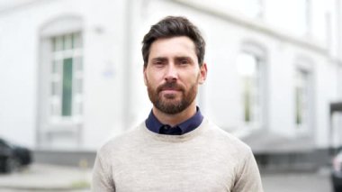 Şehir ortamında gülümseyen kendine güvenen sakallı bir adamın portresi. Bulanık şehir geçmişine karşı günlük kıyafetler giyen iş adamı, profesyonelliği aktarıyor. Mutlu ve yakışıklı erkeğin kafasından.