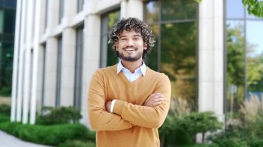 Portre gülümseyen genç yakışıklı adam modern ofis binasının önünde duruyor özgüven, başarı, pozitif tavır işleri, liderlik. Kıvırcık saçlar, kameraya akıllı bakışlar.