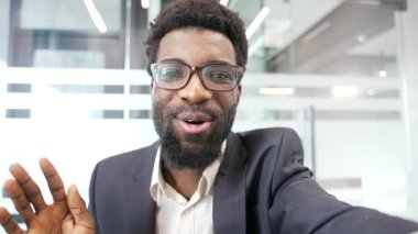 POV, resmi takım elbiseli gülümseyen Afro-Amerikalı bir işadamı iş yerinde otururken bir video görüşmesinde selfie çekerken telefonla konuşuyor. Siyah adam kameraya bakarak iletişim kuruyor. Çevrim içi sohbet