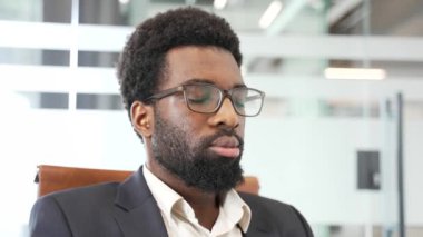 Modern ofis koltuğunda oturan Afro-Amerikan erkek profesyonel, gözleri kapalı, gözlük ve takım elbise takıyor. İş yerindeki farkındalık, rahatlama ve stres rahatlama konsepti, kapalı alanda sükunet