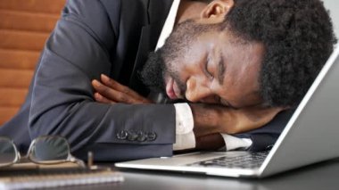 Çok çalışan Afrikalı Amerikalı iş adamı iş yerinde uyuyakalmış. Uykulu yorgun zenci işçi kafası masanın üzerine uzanmış gözlerini kapatmış, uyukluyor. Kapat.