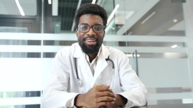 Webcam görüntüsü. Beyaz önlüklü kendine güvenen Afrikalı Amerikalı doktor kameraya bakarak teletıp seansına katıldı. Erkek doktor konferansta uzaktan iletişim kuruyor.