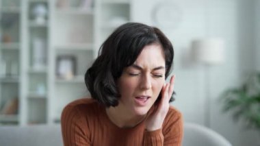 Kulak ağrısı. Hasta genç kadın evdeki oturma odasında kanepede otururken kulak ağrısından muzdarip. Üzgün kadın parmaklarıyla kulağına dokunuyor. Amcası, kiremitleri, egzaması, kulak hastalıkları ya da kulak iltihabı var.