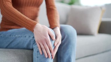 Kapatın. Oturma odasındaki kanepede otururken kadın elleri diz kaslarına masaj yapıyor. Genç bir kadın, diz eklem ağrılarından muzdarip. Yürüyemiyor, hasta olamıyor ve kramp giremiyor.