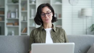 Gözlüklü kendine güvenen genç bir kadın evdeki oturma odasındaki koltukta dizüstü bilgisayarla konuşuyor. Serbest çalışan kadın müşteriyle istişare ediyor. Koç, online toplantıda iletişim kuruyor.