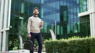 Modern cam ofis binasının önünde elinde kahve fincanı ve evrak çantası olan sıradan giyinmiş bir işadamı, başarıyı ve sabah rutinini simgeliyor. Kentsel ortam profesyonel atmosferi yansıtıyor