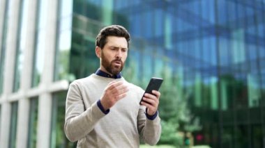 Şehir ortamında telefonla kötü haber okurken kafa karışıklığı veya endişeyi dile getiren bir iş adamı. Hüsrana uğramış bir adam dışarıda akıllı telefona bakıyor ve modern binanın önünde nahoş bir mesaj veriyor.