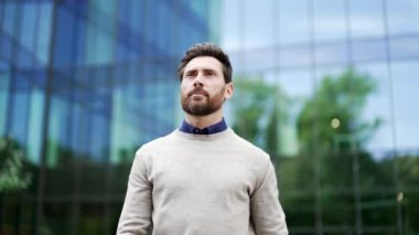 Modern cam ofis binasının yanında duran kendine güvenen bir iş adamı. Profesyonel görünüş ve düşünceli ifade başarıyı iletir. Başarılı girişimci şehrin iş bölgesine yürür.