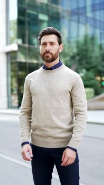 Dikey video. Kendine güvenen işadamının portresi kollarını kavuşturarak gülümsüyor ve şehir caddesinde kameraya bakıyor. Sıradan giyinen yakışıklı erkek, başarıyı ve pozitifi simgeler.