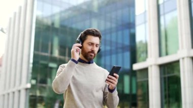 Kendine güvenen erkek profesyonel şehir ortamının dışında yürüyor, kulaklıkla müzik dinliyor ve akıllı telefon tutuyor. Şehir sokaklarında iş hayatı ve teknolojiyi gün boyunca gözler önüne serer.