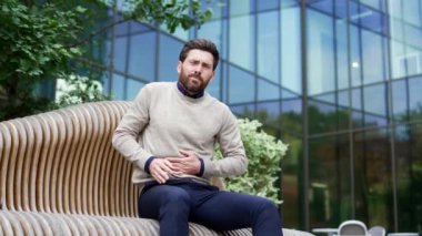 Modern binanın dışında eşsiz bir bankta oturan olgun bir adam mide ağrısı belirtileri gösteriyor. Sinirli erkek mide ekşimesi, mide iltihabı ya da zehirlenme var. Yüzünde endişe ve rahatsızlık vardı. Stres, sağlık sorunları