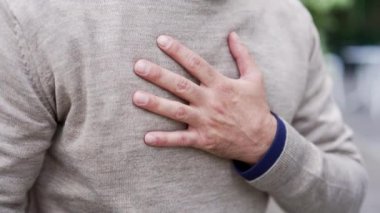 Yetişkin bir erkek göğsünü acı ya da rahatsızlık ifadesi ile tutuyor. Kazaklı adam kalp krizi geçiriyor. Endişe, sağlık, şehir sokağında potansiyel kalp sorunu. Eller yukarı.