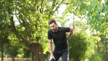 Sırt ağrısı, spor sakatlığı, şehir parkında sabah koşusu sırasında kas spazmı geçiren bir sporcu. Yetişkin sakallı koşucunun sırt ağrısı ve doğada egzersiz yaptıktan sonra sorunu var.