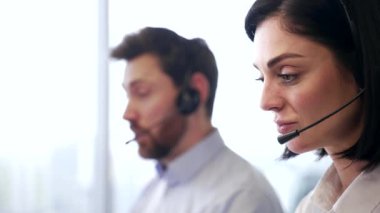 Modern ofis ortamında çalışan kulaklıklı, gülümseyen kadın müşteri hizmetleri temsilcilerinin başkanını kapatın. Bir grup şirket çalışanı merkez ajanları ile görüntülü konuşma yapıyorlar. Yan görünüm