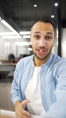 POV dikey. Gülümseyen Afro-Amerikan iş adamı iş yerindeki telefonla video görüşmesinde konuşuyor. Siyah işçi el sallayarak kameraya bakıyor. Bir müşteri veya iş ortağıyla çevrimiçi sohbet