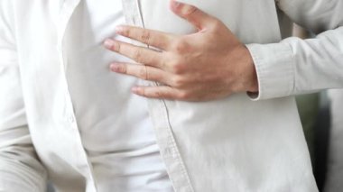 Kapatın. Erkek eli, masaj sandığı tutuyor. Beyaz gömlekli genç adam evdeki oturma odasında kanepede otururken kalp krizi geçiriyor. Hasta erkek derin nefes alıyor. Acil tıbbi yardıma ihtiyacı var.