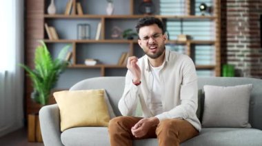 Kulak ağrısı. Hasta genç bir adam evdeki oturma odasındaki koltukta otururken kulak ağrısından muzdarip. Üzgün erkek parmaklarıyla kulağına dokunuyor. Amcası, kiremitleri, egzaması, kulak hastalıkları ya da kulak iltihabı var.