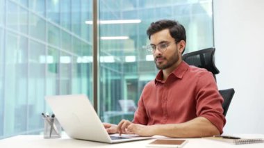 Modern ofis masasında dizüstü bilgisayarda yazan odaklanmış profesyonel bir erkek. Gözlüklü bir iş adamı, işine odaklanıyor. Yakışıklı sakallı erkek işçi bilgisayarda çalışıyor.