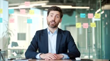Webcam görüntüsü. Ofiste oturan kameraya bakan yakışıklı bir iş adamı. Resmi takım elbiseli bir adamın iş görüşmesi var. Uzaktan konuşuyor. İnternet konferansında iletişim kuruyor.