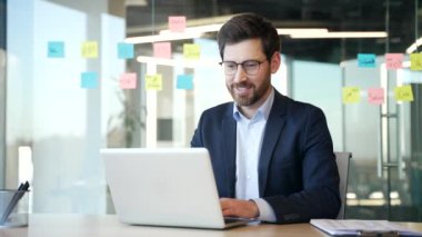 Modern ofiste dizüstü bilgisayarla çalışan bir iş adamı. Gülümseyen adam modern iş yerinde iş stratejisi planlıyordu. Bilgisayar uygulaması ve bankacılık alanında çalışan gözlüklü bir yönetici