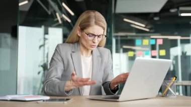 Takım elbiseli kızgın bir iş kadını iş yerindeki iş yerinde bilgisayarında oturup video görüşmesi yapıyor. İş meseleleri ve sorunlar hakkında astlarıyla hayal kırıklığına uğramış kadın yönetici kavgası