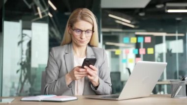 Sinirli iş kadını, iş yerindeki masasında oturan cep telefonundaki yazılımın kötü performansından şikayetçi. Kadın akıllı telefon, internet ve hizmet işinden memnun değil.