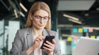 Ceketli düşünceli bir iş kadını iş yerindeki iş yerinde cep telefonu kullanıyor. Odaklanmış kadın yönetici başvuruda çalışıyor, internette sohbet ediyor ya da projeyi düşünüyor. Kapat.