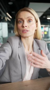 POV dikey. İş kadını, ofisteki bir iş yerinde telefonla video görüşmesi yapıyor. Kameraya bakan kadın selfie çekiyor, müşteriyle konuşuyor ya da iş ortağıyla sohbet ediyor.