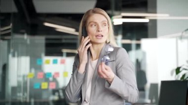Modern bir ofiste dikilirken cep telefonuyla konuşan ceketli, kendine güvenen bir iş kadını. Meşgul bayan yönetici iş ortağıyla iş meselelerini tartışıyor ya da bir müşteriyle sohbet ediyor.