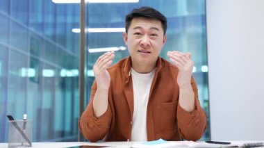 Webcam görüntüsü. Kendine güvenen Asyalı iş adamı iş yerindeki kameraya bakarak bir video görüşmesi yapıyor. Girişimcinin bir iş toplantısı var. Müdür çevrimiçi bir konferansta uzaktan konuşuyor.